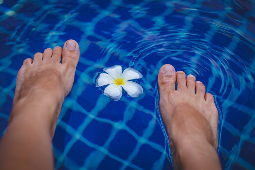 Image of feet and a flower floating on the top of clear pool with blue tile. Ionic detoxification foot bath services offered at the Karlfeldt Center of Idaho.