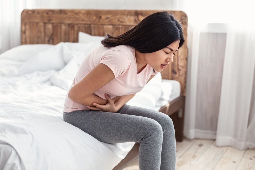 Woman sitting on the edge of her bed holding her gut.